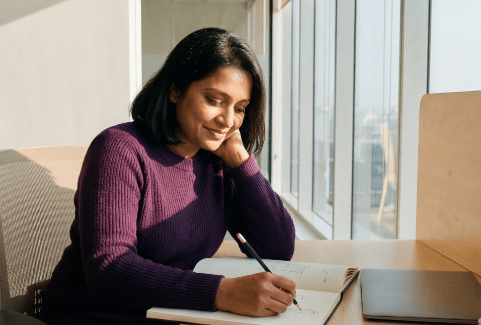 Person sitting at a desk writing in a notebook and smiling, representing tracking ADHD medication progress and treatment goals